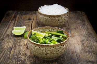 Green thai curry with broccoli, pak choi, snow peas, baby spinach, lime and bowl of rice in the background - LVF06979