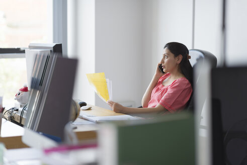 Woman holding papers on telephone call at office desk - CUF06398