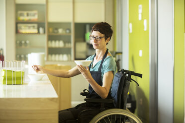 Woman in wheelchair, working in restaurant, holding bowl of food - CUF06408