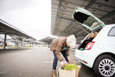Ältere Frau auf dem Parkplatz, die Einkäufe in den Kofferraum des Autos lädt - CUF06412
