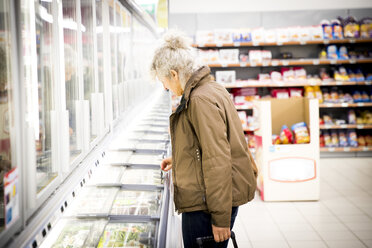 Ältere Frau im Supermarkt, schaut in die Kühltruhe - CUF06415