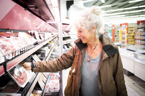 Ältere Frau im Supermarkt, die sich die Abteilung für gekühltes Fleisch ansieht - CUF06422