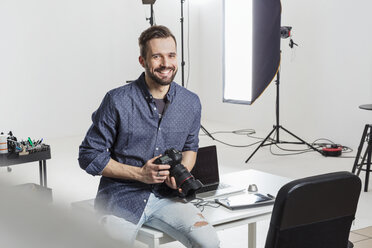 Portrait of male photographer sitting on desk in photography studio - CUF06437