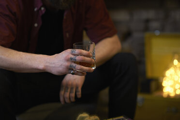 Mittelteil eines Mannes mit tätowierten Fingern, der einen Becher mit Spirituosen in einem Gasthaus hält - CUF06470