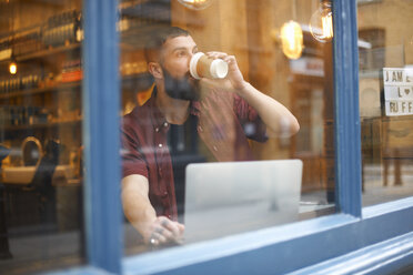 Blick aus dem Fenster auf einen jungen Mann, der in einem Café Kaffee trinkt - CUF06475