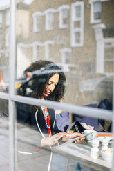 Fensteransicht einer Frau, die in einem Café ein digitales Tablet benutzt - CUF06488