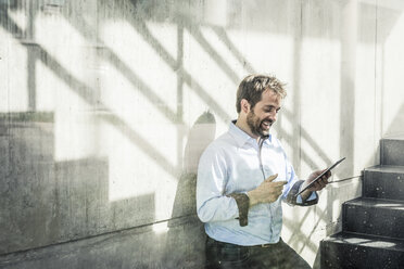 Geschäftsmann im Treppenhaus eines Büros mit Blick auf ein digitales Tablet - CUF06515