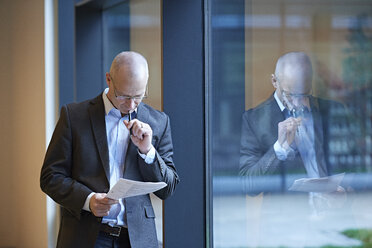 Mature businessman by office window reading paperwork - CUF06533