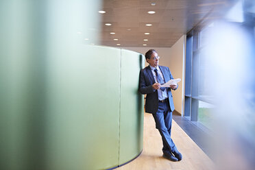 Mature businessman leaning against wall looking through office window - CUF06535