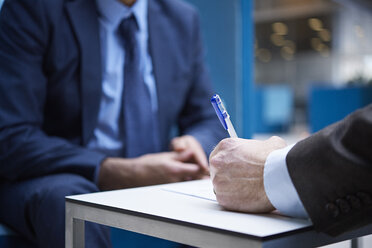 Geschäftsleute beim Unterzeichnen von Papieren im Atrium eines Büros, ausgeschnitten - CUF06539