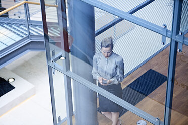 High angle view of businesswoman looking at smartphone on office stairway - CUF06557