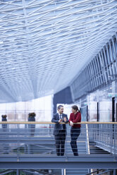 Businessman and woman talking in office atrium - CUF06563