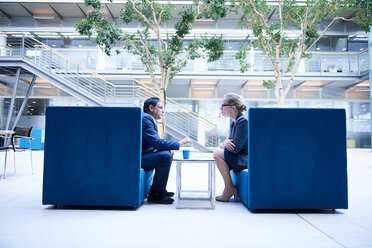 Businesswoman and man at meeting in office atrium armchairs - CUF06575