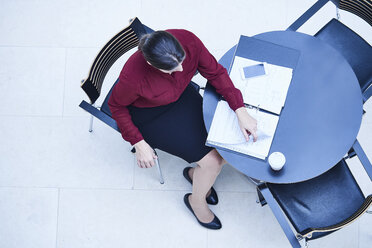 Draufsicht auf eine Geschäftsfrau, die an einem Tisch im Atrium eines Büros Papierkram liest - CUF06578