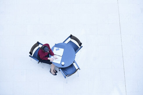 Draufsicht auf eine Geschäftsfrau, die an einem Tisch im Atrium eines Büros Papierkram liest - CUF06579