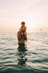 Vater trägt seine kleine Tochter auf den Schultern im Meer bei Sonnenuntergang - GEMF01972