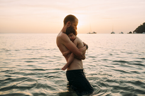 Mann, der seine kleine Tochter auf dem Arm trägt, während er im Meer watet, lizenzfreies Stockfoto