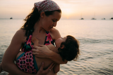 Mutter hält kleine Tochter auf ihren Armen vor dem Meer bei Sonnenuntergang - GEMF01979