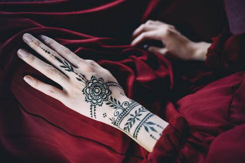 Hand einer Frau mit Henna-Tätowierung auf rotem Tuch - GEMF01981