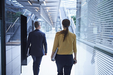 Rear view of businesswoman and man walking through office atrium - CUF06595