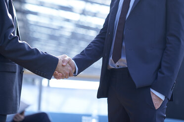 Mid section of two businessmen shaking hands in office atrium - CUF06627