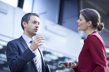 Businessman and woman talking in office atrium - CUF06628