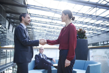 Businessman and woman shaking hands in office atrium - CUF06631