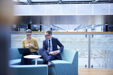 Businessman and woman looking at laptop in office atrium - CUF06639