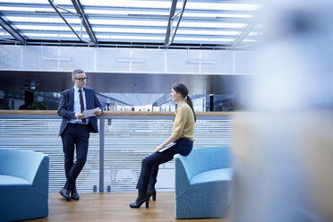 Businessman and woman having discussion in office atrium - CUF06643