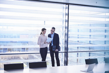 Businesswoman and man reading paperwork for boardroom table - CUF06718