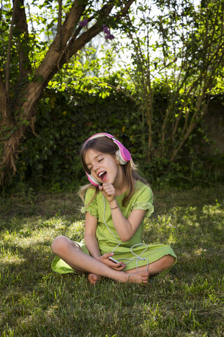 Portrait of girl sitting on meadow listening music with headphones and smartphone stock photo