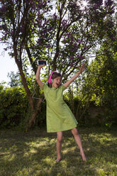 Singing girl with headphones and smartphone dancing in the garden - LVF06982