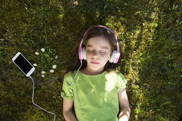 Mädchen liegt auf einer Wiese und hört Musik mit Kopfhörern und Smartphone - LVF06986