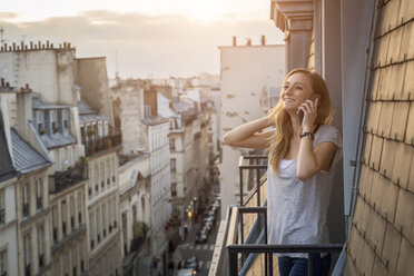 Frankreich, Paris, Porträt einer lächelnden, telefonierenden Frau auf einem Balkon am Abend - JUNF01046