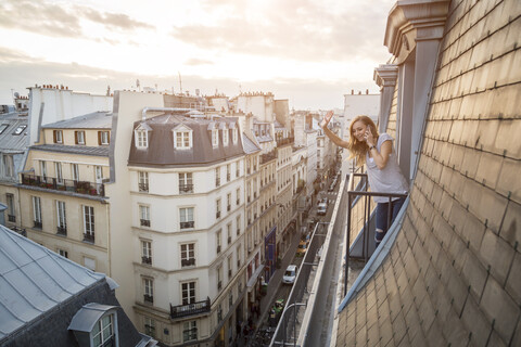 Frankreich, Paris, winkende Frau am Telefon, die auf einem Balkon steht und nach unten schaut, lizenzfreies Stockfoto