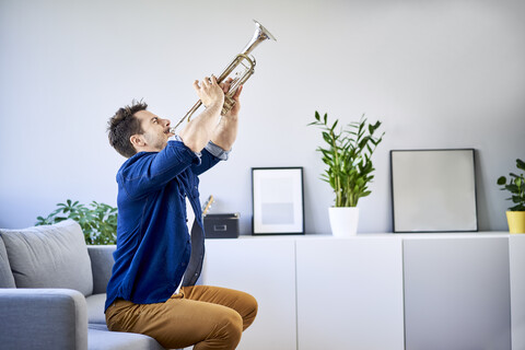 Man sitting on couch playing trumpet stock photo