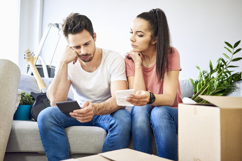 Serious couple sitting on couch in new home checking bills - BSZF00399