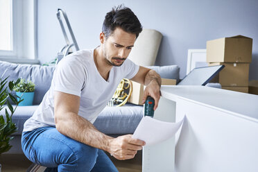 Mann liest Anweisungen beim Zusammenbau von Möbeln in einer neuen Wohnung - BSZF00409