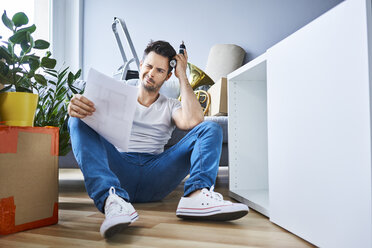 Frustrierter Mann liest Anleitungen beim Zusammenbau von Möbeln in einer neuen Wohnung - BSZF00410