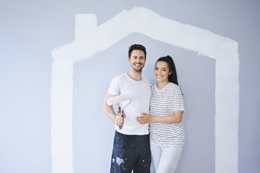 Porträt eines glücklichen Paares in einer neuen Wohnung mit Hausform an der Wand - BSZF00420