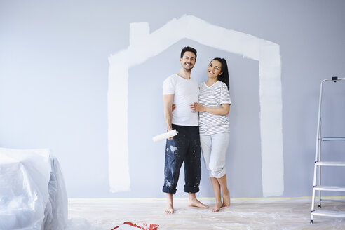Porträt eines glücklichen Paares in einer neuen Wohnung mit Hausform an der Wand - BSZF00422