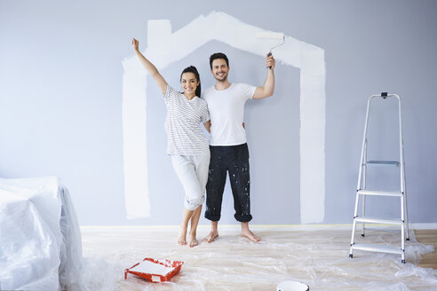 Porträt eines fröhlichen Paares in einer neuen Wohnung mit Hausform an der Wand - BSZF00423