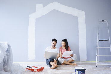 Couple sitting in new apartment using laptop - BSZF00424