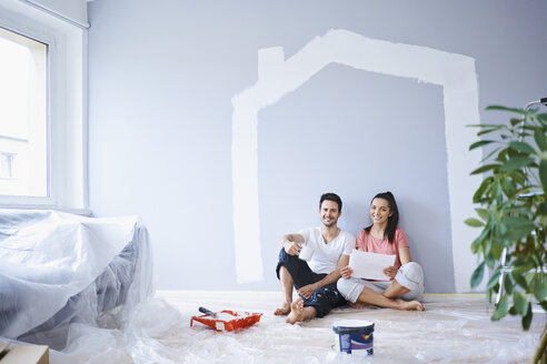 Happy couple taking break from painting walls in new apartment - BSZF00425