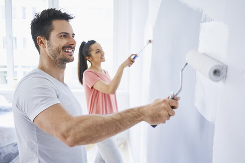 Happy couple painting wall in apartment together - BSZF00427