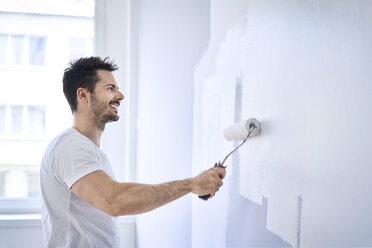 Lächelnder Mann malt Wand in Wohnung - BSZF00428