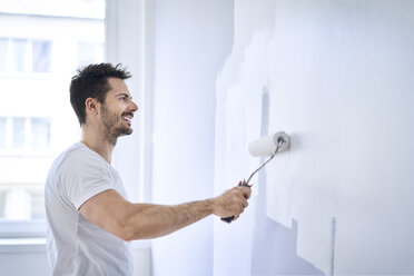 Smiling man painting wall in apartment - BSZF00428