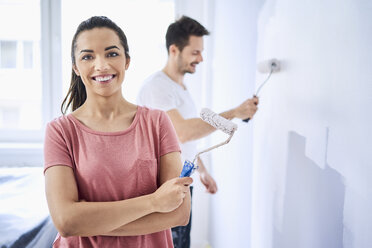 Porträt einer glücklichen Frau, die mit ihrem Freund die Wand in ihrer neuen Wohnung bemalt - BSZF00429