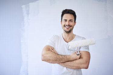 Portrait of smiling man painting wall in apartment - BSZF00430