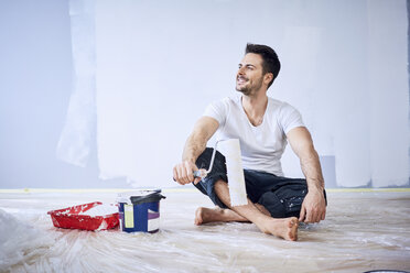 Smiling man sitting in new apartment taking a break from painting - BSZF00431